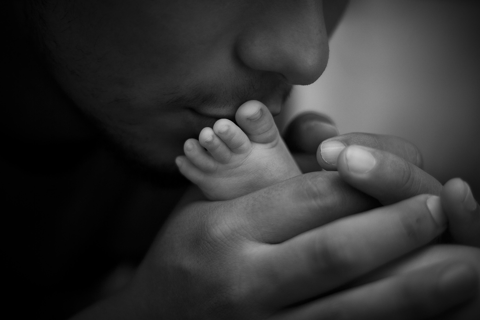 un papà bacia i piedini del suo bambino. L'Italia non sembra essere un paese per i papà