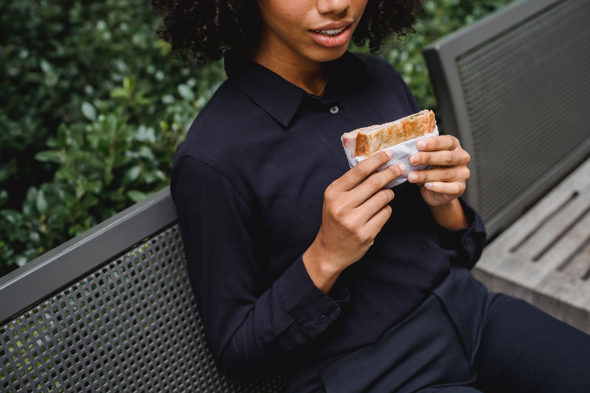 crop black woman having lunch on bench