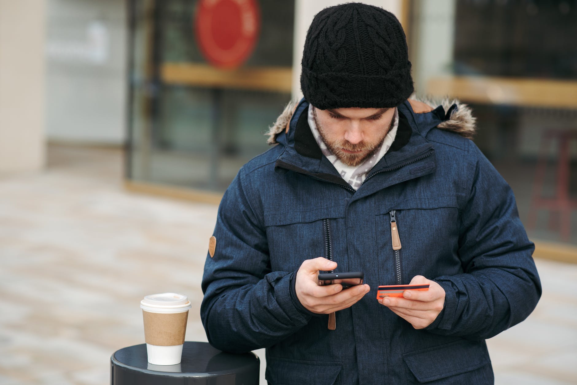 focused male holding credit card while making payment with smartphone on street